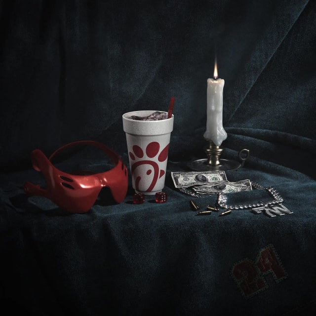 3D still life on dark velvet: red goggles, a styrofoam cup, a candle, dollar bills and dice