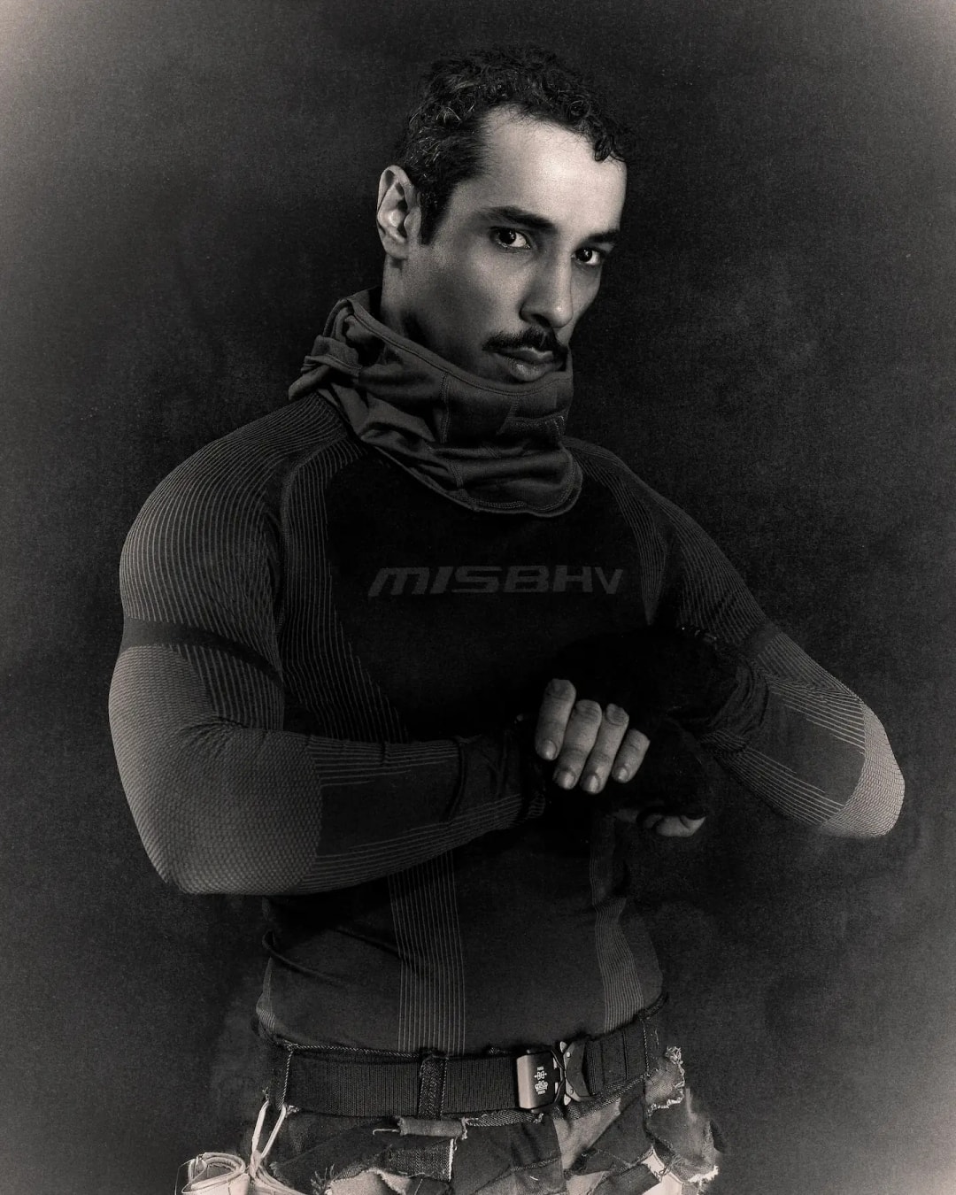 Black and white portrait of M Le Maudit in a MISBHV base layer and scarf, hands clasped in front