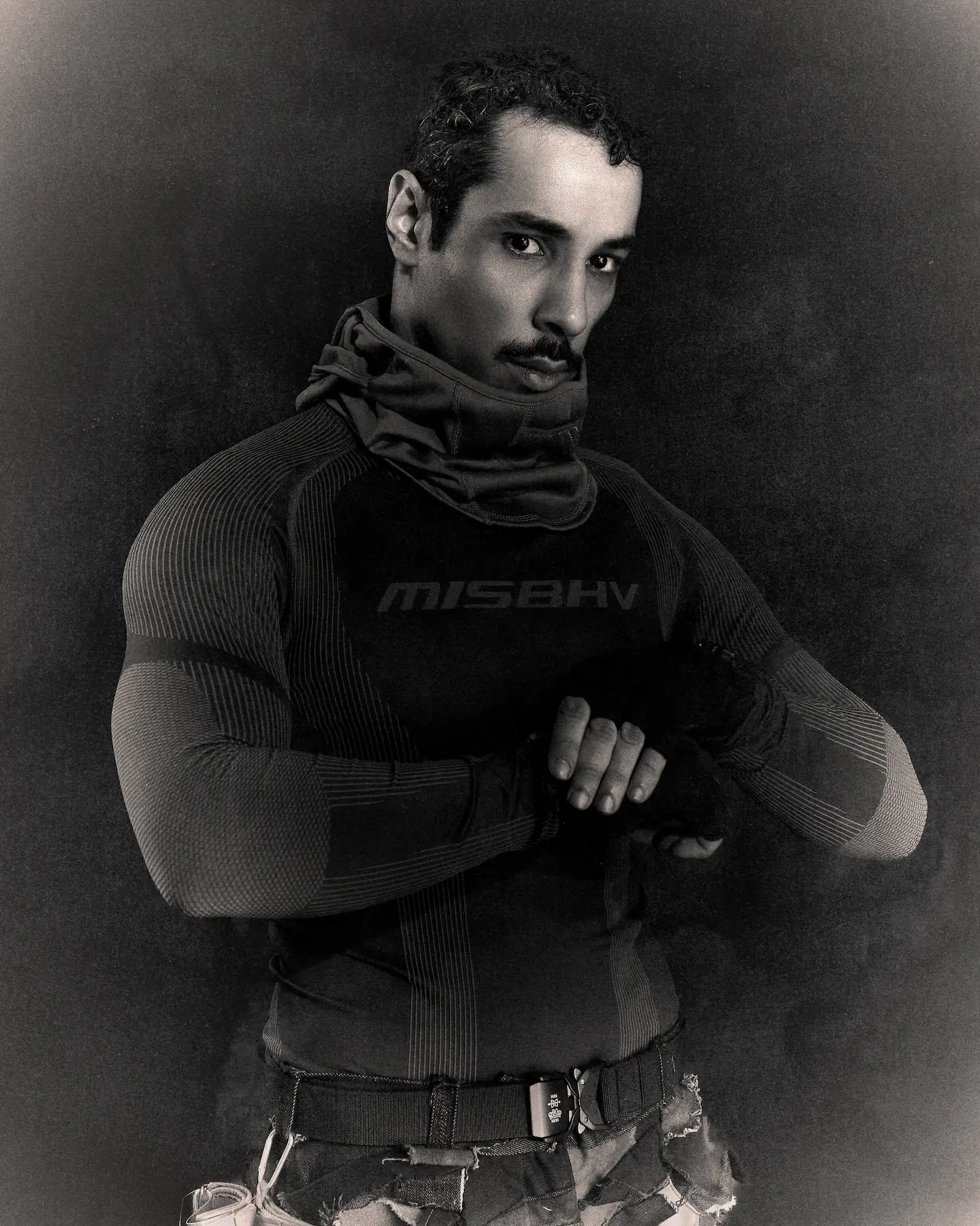 Black and white portrait of M Le Maudit in a MISBHV base layer and scarf, hands clasped in front