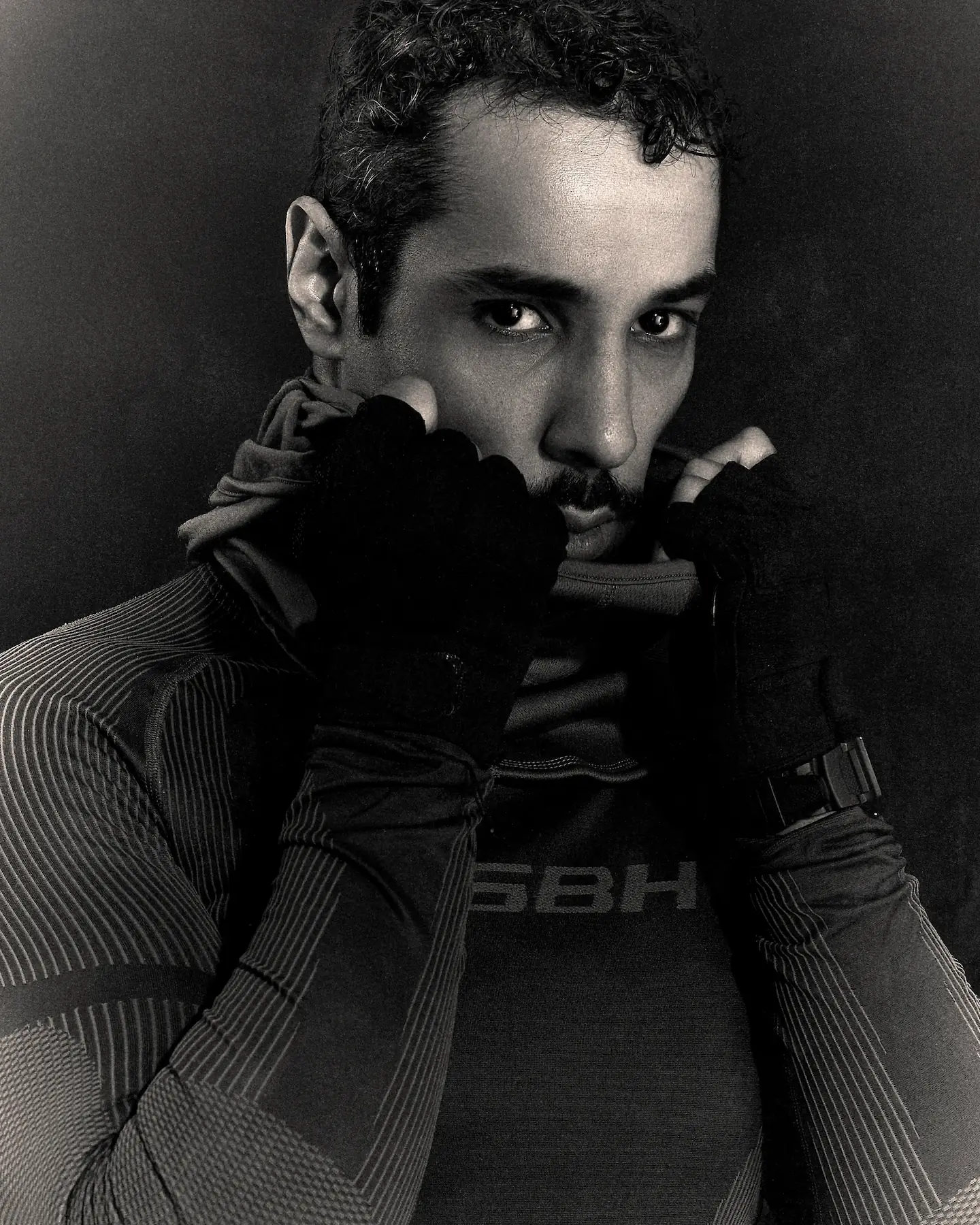 Black and white close-up of M Le Maudit in fingerless gloves, hands raised to his mouth