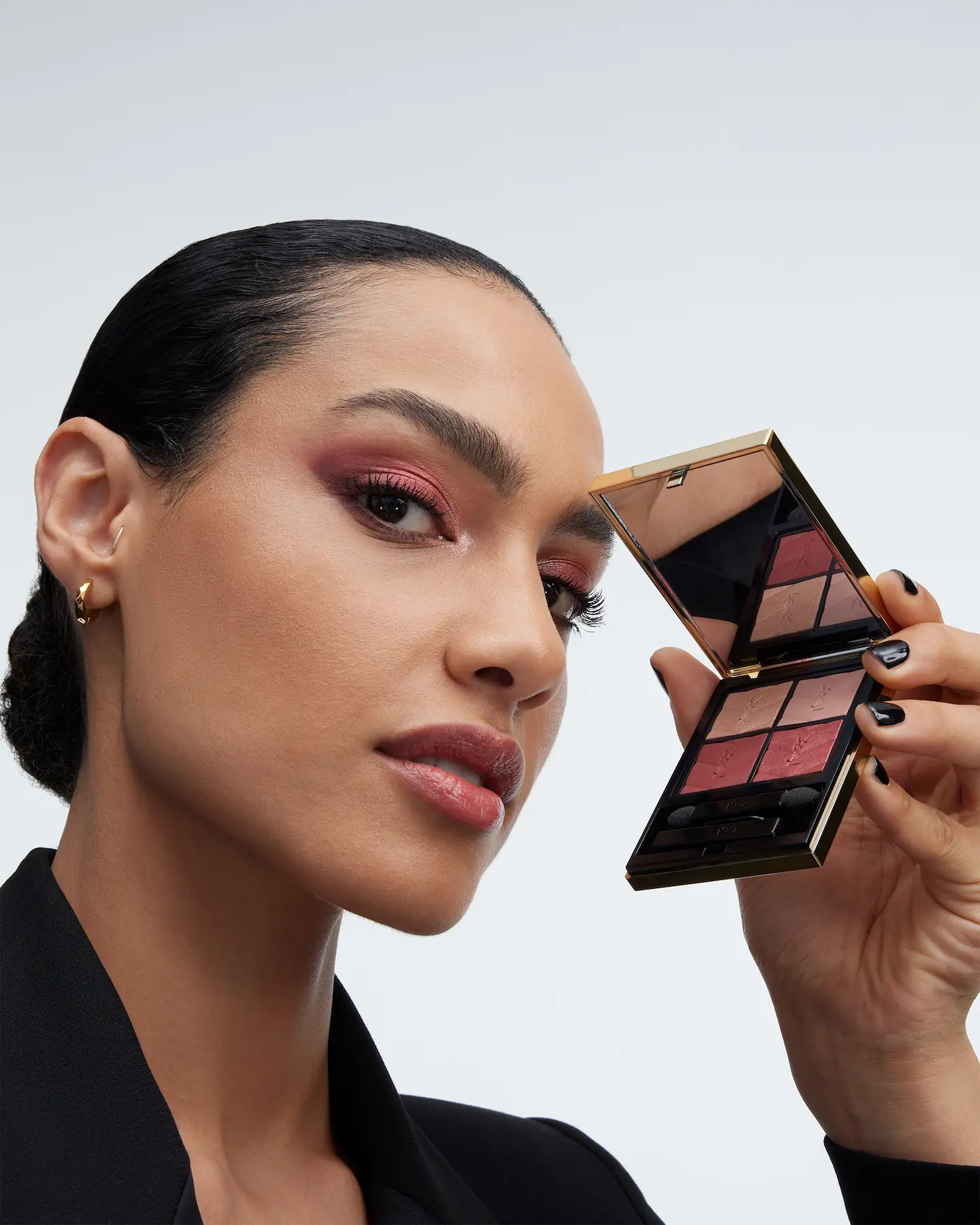 Model with pink eye makeup holding an open YSL Beauty eyeshadow palette beside her face