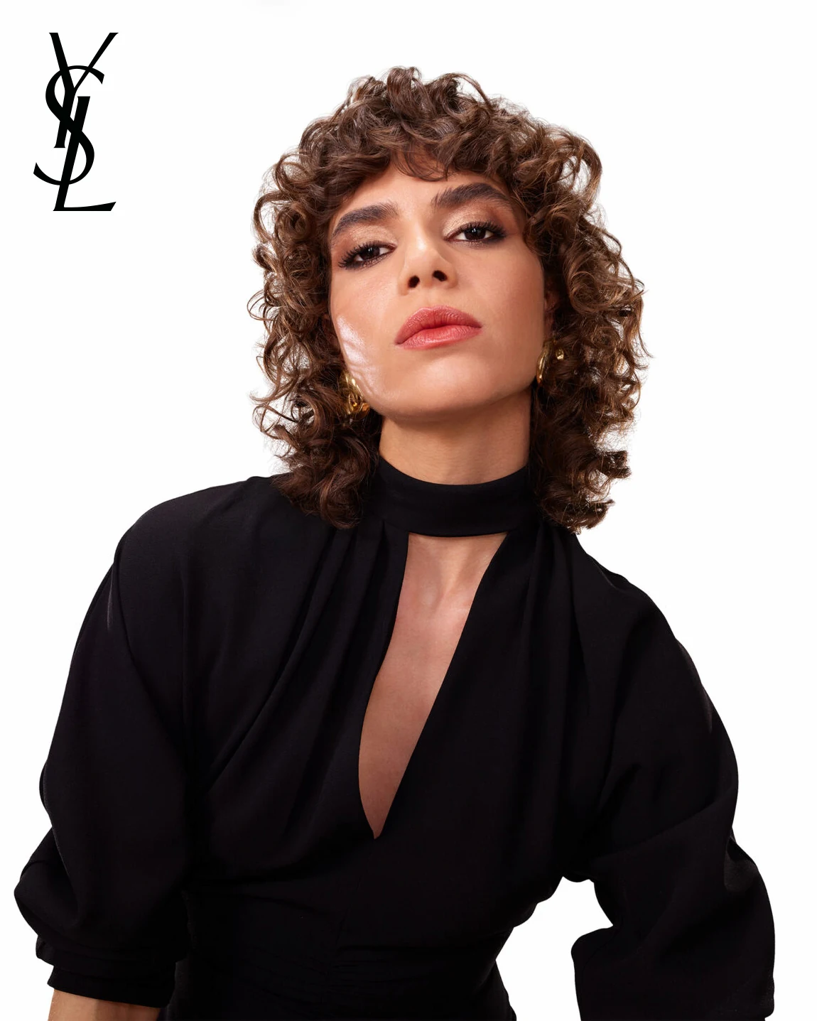 YSL Beauty portrait of a model with curly hair in a black plunging blouse, YSL logo on white